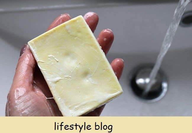 uma mão segurando uma barra de sabão de azeite amarelo sobre uma bacia. Espuma cremosa com poucas bolhas na barra